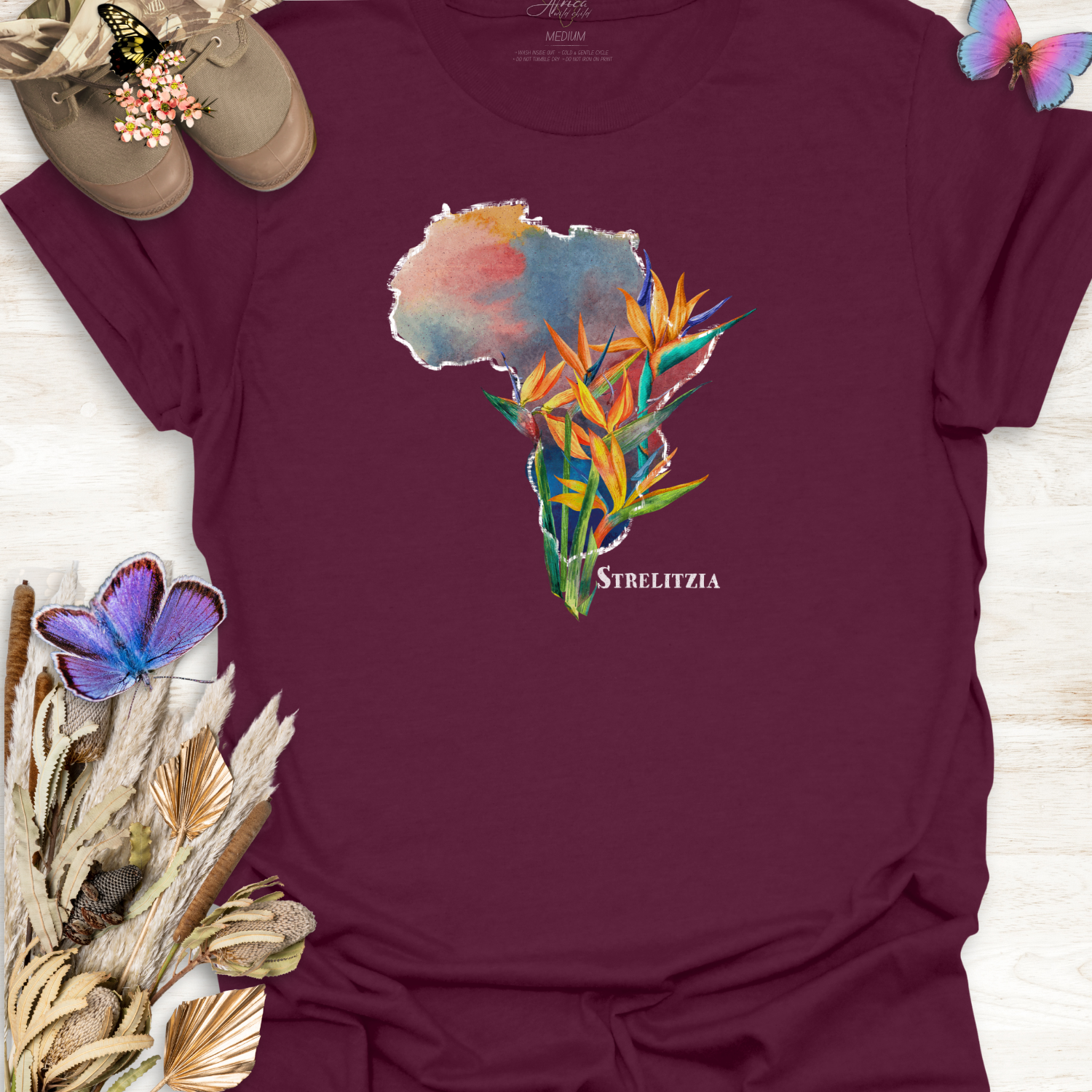 Maroon t-shirt with a colorful graphic of Africa and Strelitzia flowers on a wooden surface.