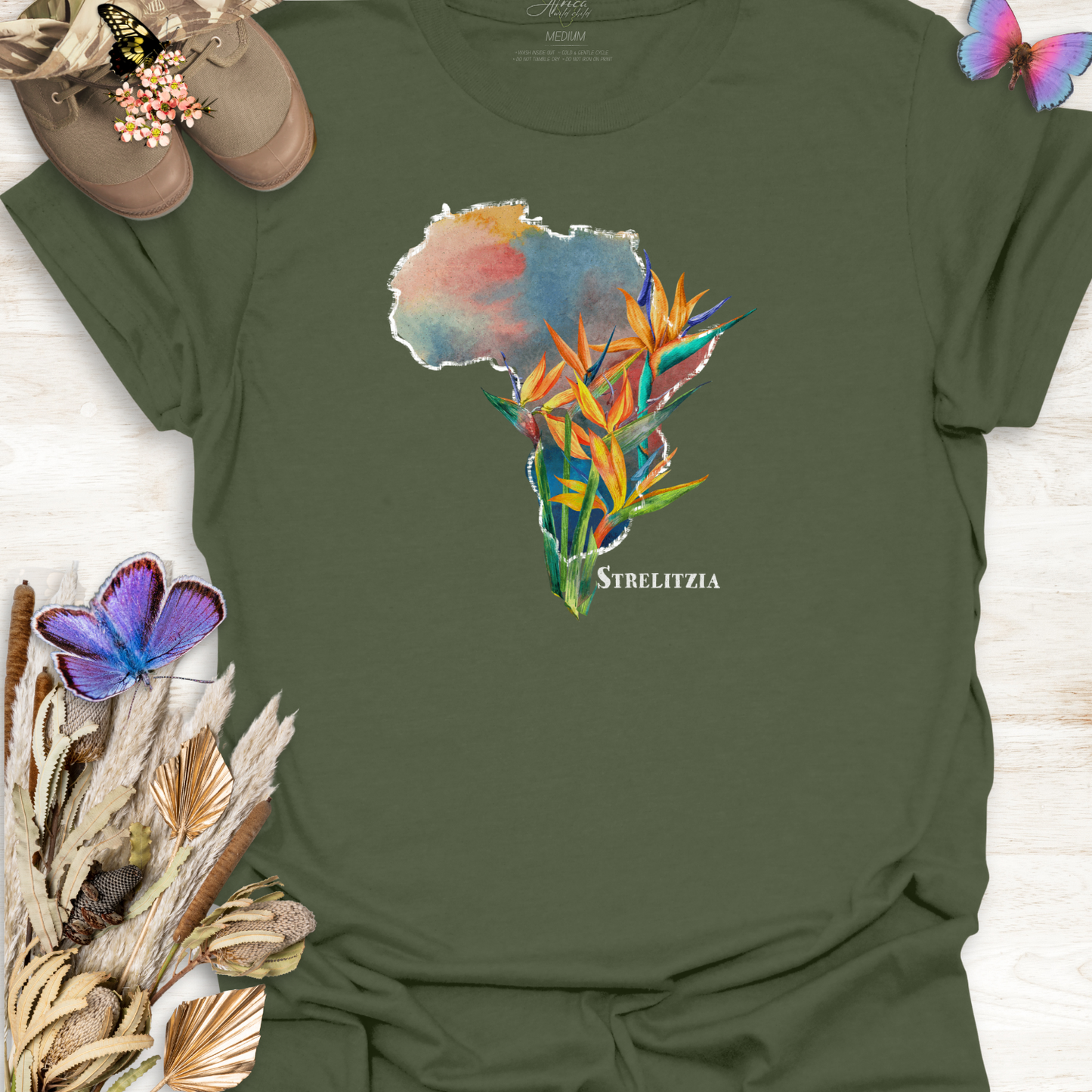 Military Green t-shirt with a colorful graphic of Africa and Strelitzia flowers on a wooden surface.
