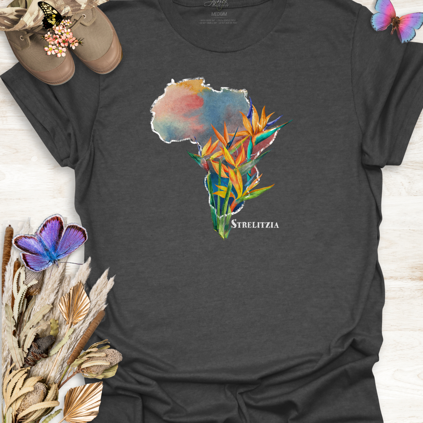 Grey t-shirt with a colorful graphic of Africa and Strelitzia flowers on a wooden surface.