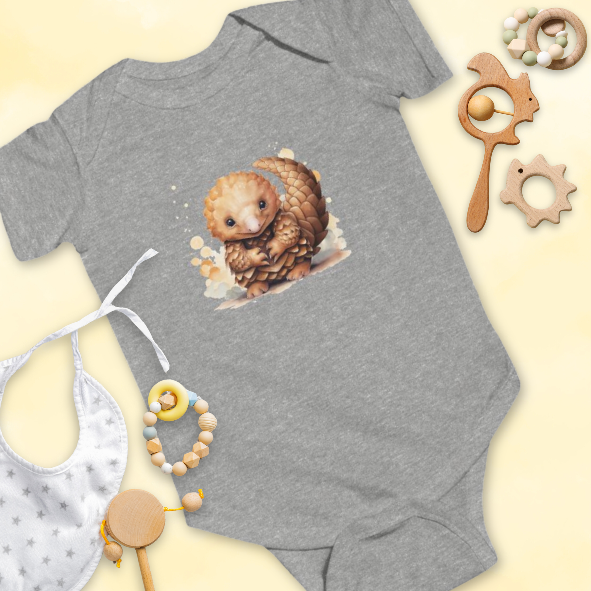 Gray baby onesie with a pangolin design, surrounded by baby items on a light yellow background.
