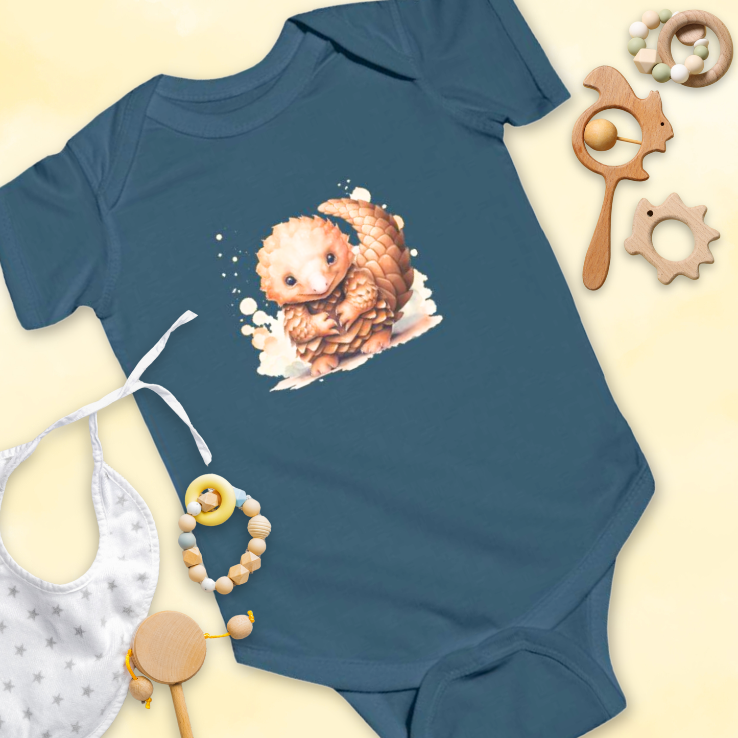 Blue baby onesie with a pangolin design, surrounded by baby items on a light yellow background.