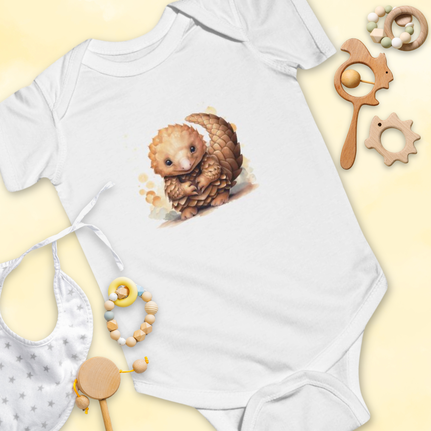 White baby onesie with a pangolin design, surrounded by baby toys on a light yellow background