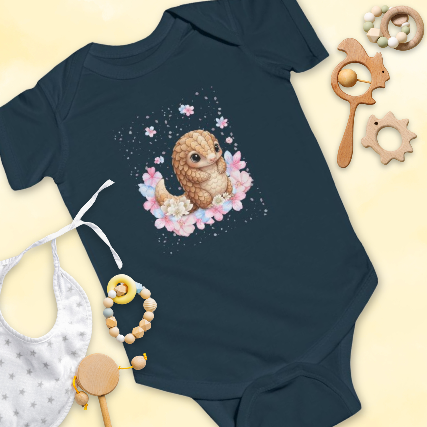 Navy blue baby onesie with a cartoon pangolin & flower design, surrounded by baby toys on a light yellow background.