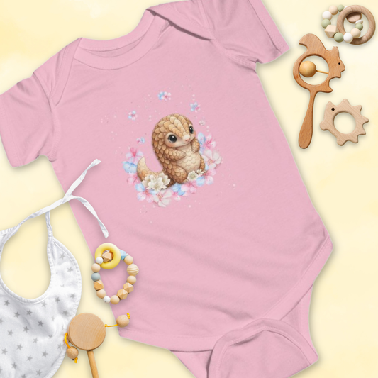 Pink baby onesie with a cartoon pangolin & flower design, surrounded by baby toys on a light yellow background.