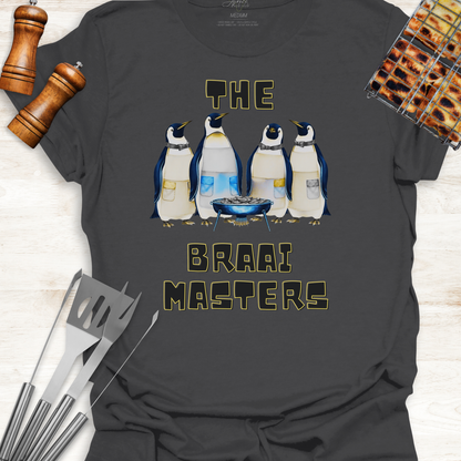 Gray t-shirt with penguin design and 'The Braai Masters' text on a wooden surface with grill tools.