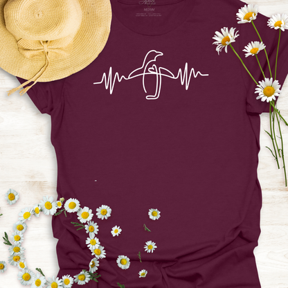 Maroon wildlife t-shirt with a penguin  heartbeat design, surrounded by daisies and a straw hat on a light wooden surface.