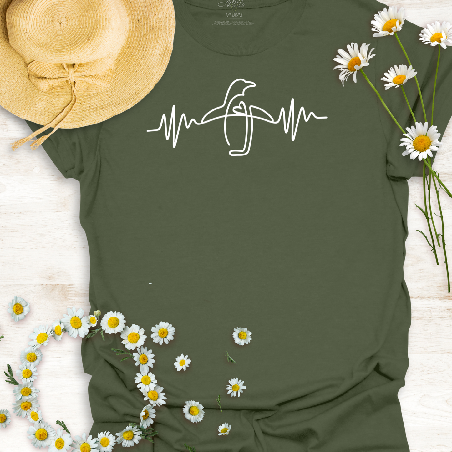 Green wildlife t-shirt with a penguin design and heartbeat line, surrounded by daisies and a straw hat.