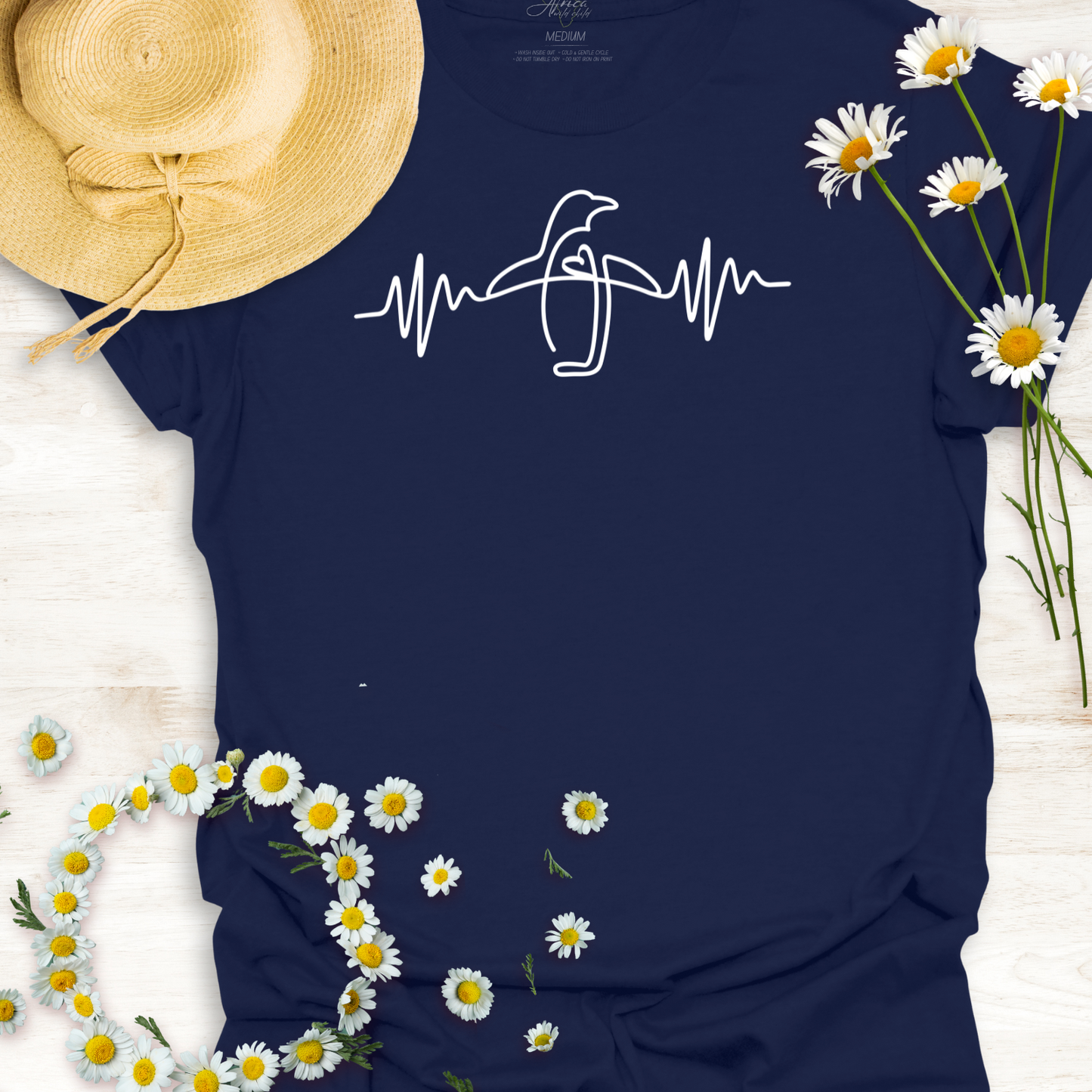 Navy blue wildlife t-shirt with a penguin  design and heartbeat line, surrounded by daisies and a straw hat.
