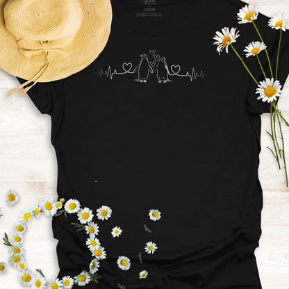 Black  t-shirt with hearts on a heartbeat line with penguins designs, a straw hat, and daisies on a light wooden surface.